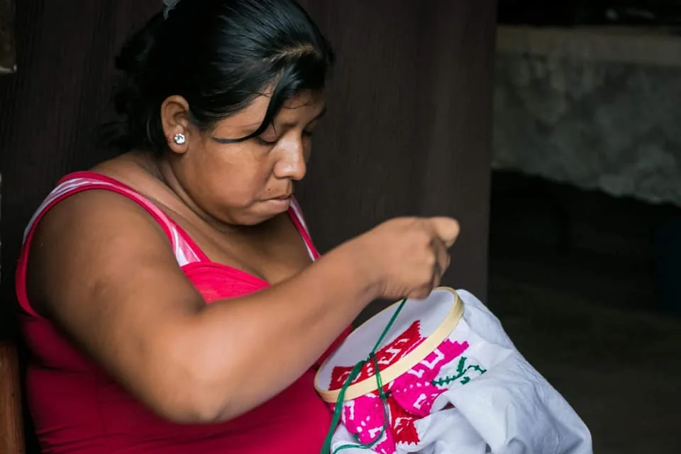 Una mujer borda una prenda a mano
